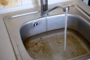 Clogged kitchen sink with dirty water and running tap.