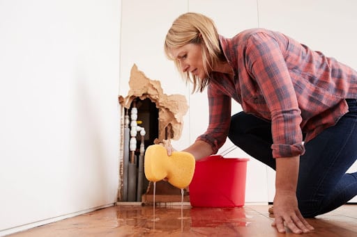 Water damage cleanup in action, as a woman uses a sponge to soak up water.