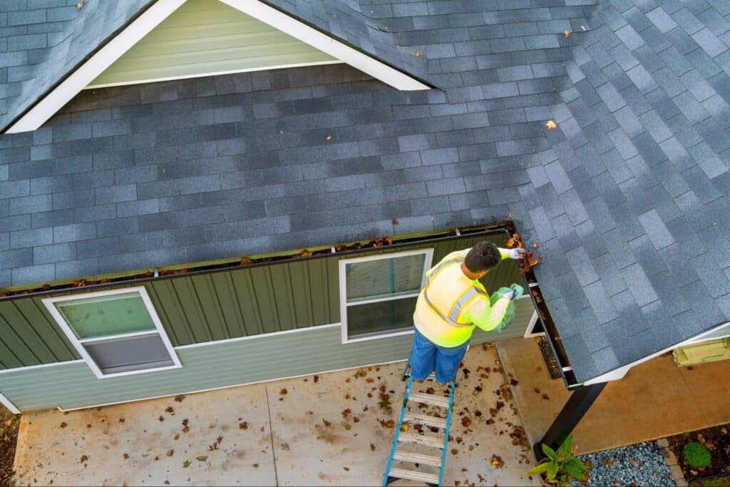 Worker cleaning gutters to ensure proper roof drainage and maintenance.