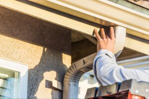 Handyman installing gutters on a house for effective water drainage and home protection.