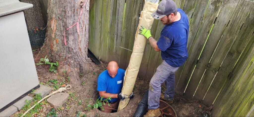 Hydromax Plumbers repairing a sewer line in a residential yard with tools and equipment.
