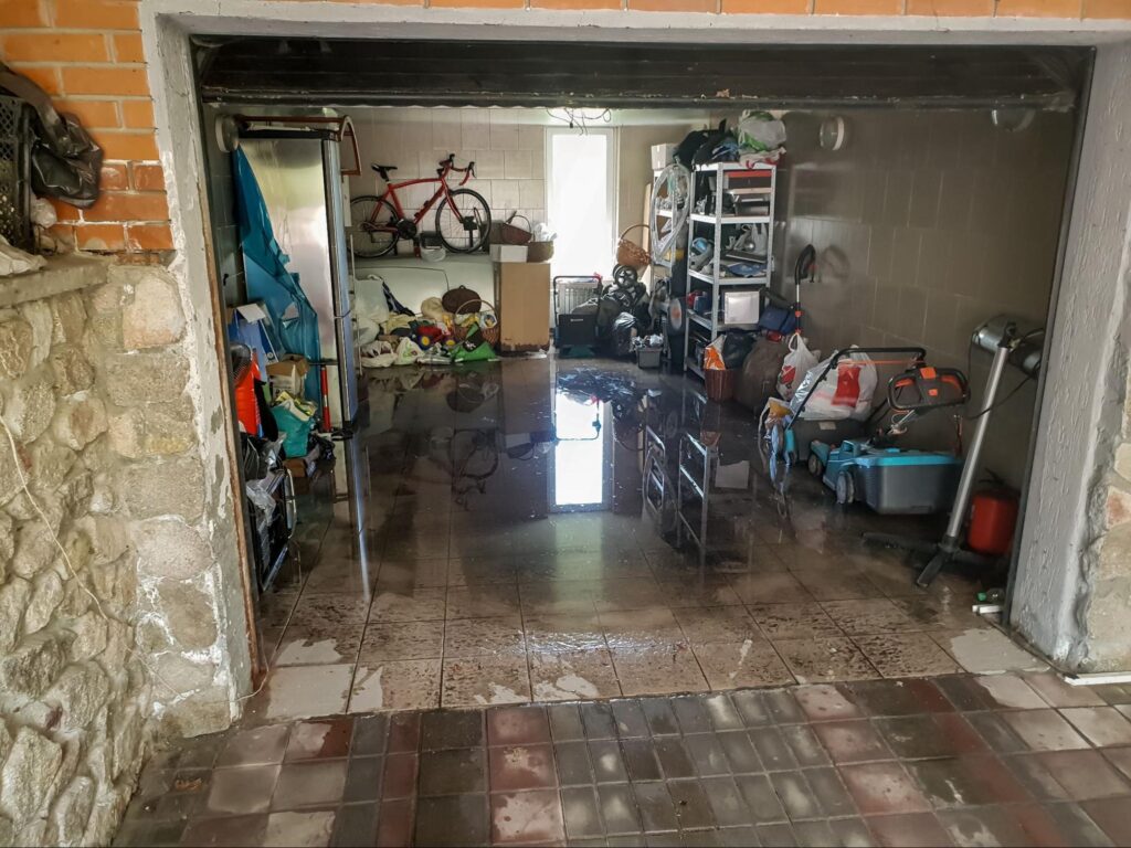 Flooded garage with water damage and cluttered storage items visible inside.