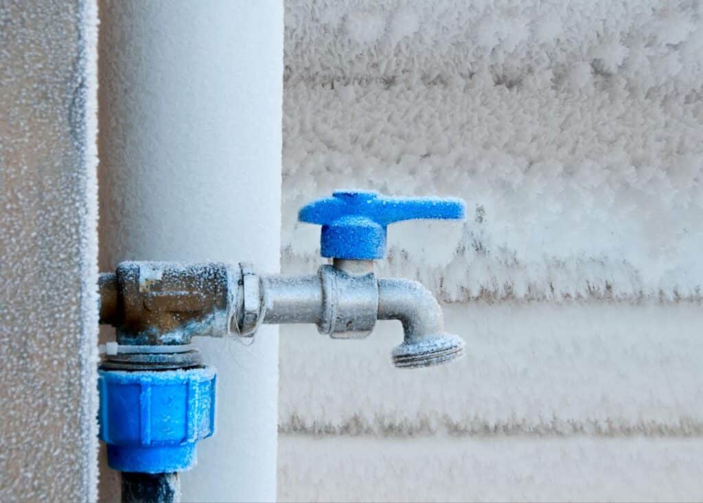 Frost-covered outdoor faucet with a blue handle conveying winter plumbing challenges.