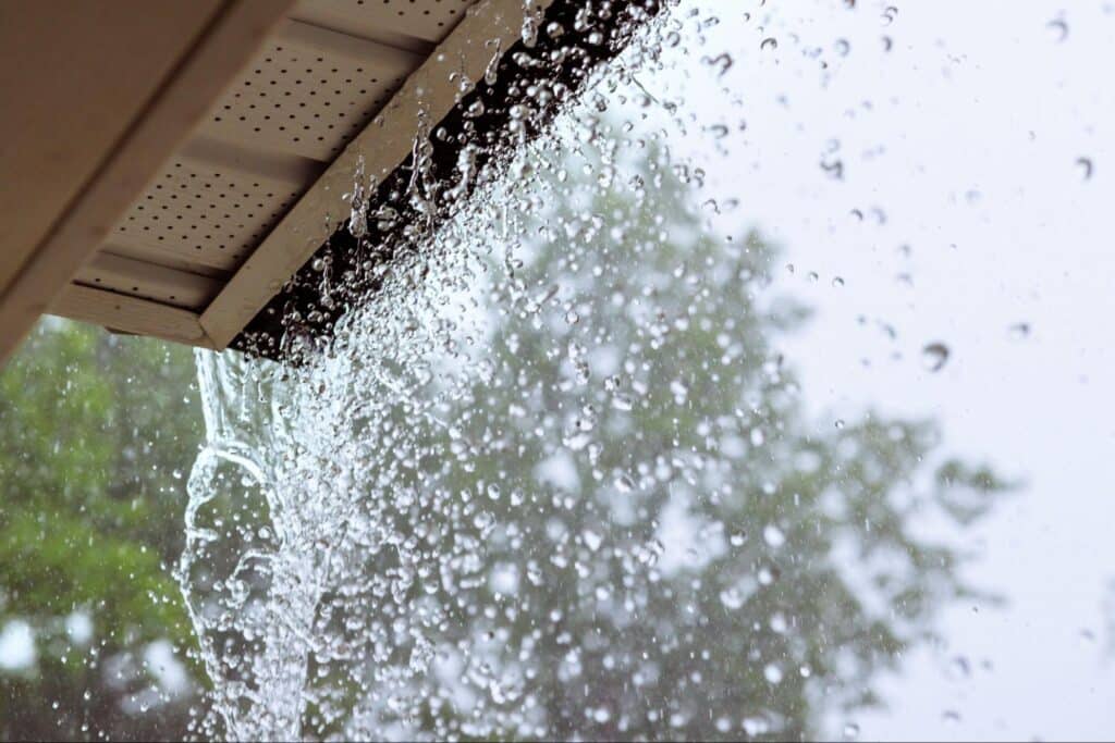 Rainwater cascades from a roof due to improper downspout placement