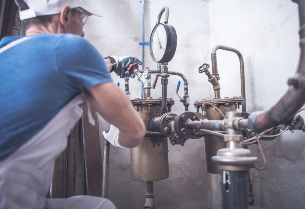 Technician performing regular plumbing maintenance to check pressure gauges on industrial plumbing system.