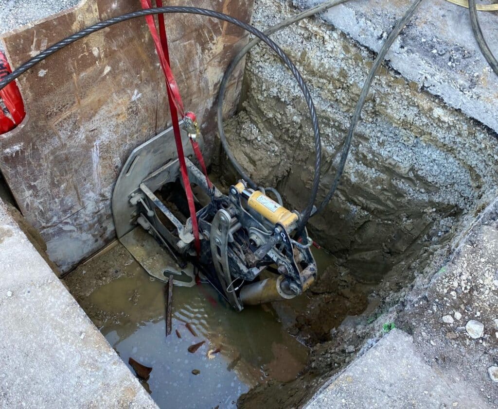 Construction machinery in a deep excavation site with water accumulation from Pipe Bursting.