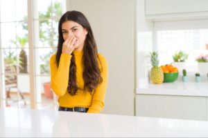 Woman in a yellow shirt smiles in a bright, modern kitchen with fresh fruits.