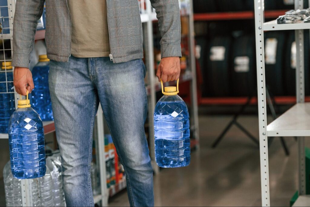 Person carrying two large bottles of fresh water in a store aisle.