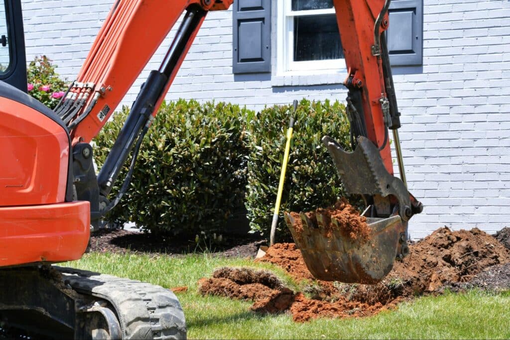 Excavator performing sewer repairs in residential yard.