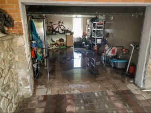 Water-damaged garage filled with materials and a bicycle, highlighting cleanup challenges.