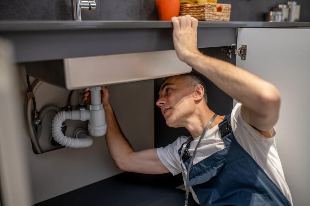 Plumber inspecting kitchen sink pipes for repairs and maintenance solutions.